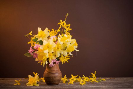 Foto de Flores amarillas y rosadas en jarra sobre fondo marrón - Imagen libre de derechos