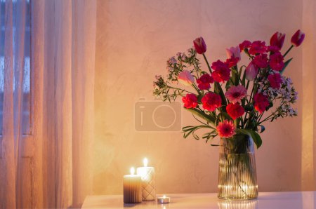 Photo for Pink flowers in glass modern vase with burning candles in white interior - Royalty Free Image