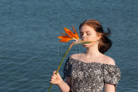 Foto de Mujer joven con flor exótica naranja en el mar fondos - Imagen libre de derechos