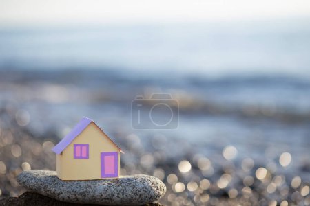 Foto de Una pequeña casa de papel sobre el telón de fondo del mar al atardecer, el concepto de servicios inmobiliarios, un sueño de una casa por el se - Imagen libre de derechos