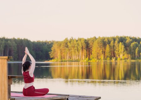 Photo for Girl doing yoga on wooden pier by lake in summer - Royalty Free Image