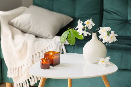 Téléchargez les photos : Branche de rhododendron blanc dans un vase et des bougies brûlantes dans l'intérieur confortable moderne - en image libre de droit