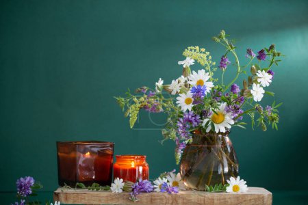 Téléchargez les photos : Fleurs sauvages dans un vase en verre brun avec des bougies allumées sur fond vert - en image libre de droit
