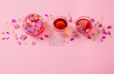 Téléchargez les photos : Thé avec pétales de rose dans une théière en verre sur fond rose - en image libre de droit