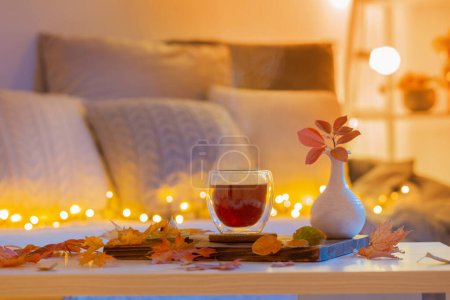 Foto de Termo vidrio con té caliente en cuarto oscuro de la noche con hojas otoñales - Imagen libre de derechos