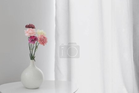 Téléchargez les photos : Belles fleurs d'oeillet dans un vase en céramique sur table blanche - en image libre de droit