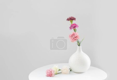 Photo for Beautiful carnation flowers in ceramic vase on white table - Royalty Free Image