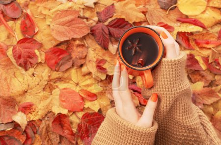 Téléchargez les photos : Mains féminines avec tasse orange de café sur fond feuilles d'automne - en image libre de droit
