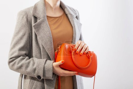 Téléchargez les photos : Femme en manteau gris avec sac à main orange sur fond blanc - en image libre de droit