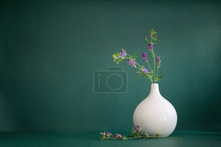 Photo for Wild purple flowers in white modern vase on green background - Royalty Free Image