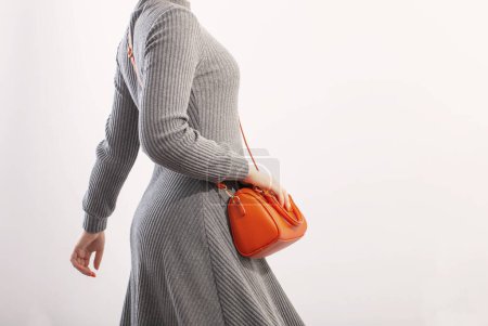 Téléchargez les photos : Femme en robe de jersey gris avec sac à main orange sur fond blanc - en image libre de droit