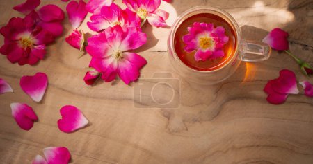 Foto de Pétalos de rosa rosa y taza de té sobre fondo de madera - Imagen libre de derechos