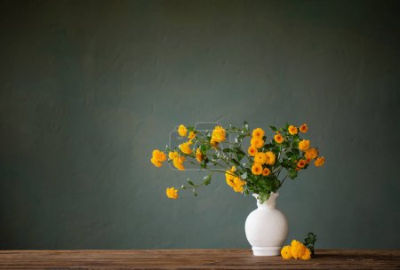 yellow chrysanthemums in white vase on background dark wall