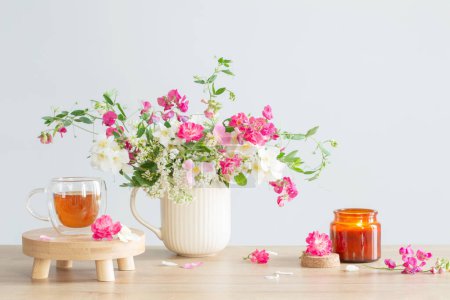 Foto de Flores de verano, velas encendidas y taza de té sobre fondo claro - Imagen libre de derechos