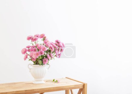 Pink chrysanthemums in white vase on white interior