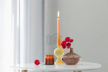Foto de Rosas rojas en jarrón con velas encendidas en el interior blanco - Imagen libre de derechos