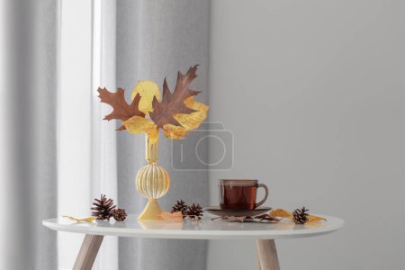 Téléchargez les photos : Tasse de thé et feuilles d'automne dans un vase en verre sur fond gris mur - en image libre de droit