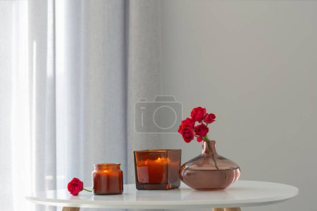 Foto de Rosas rojas en jarrón con velas encendidas en el interior blanco - Imagen libre de derechos