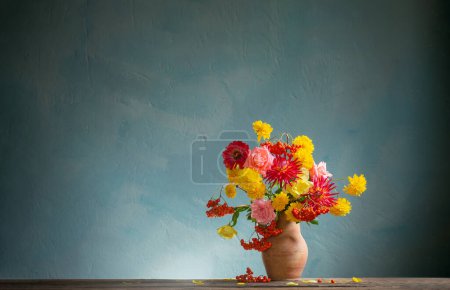 Foto de Flores rojas y amarillas en jarra a la luz del sol sobre fondo pared oscura - Imagen libre de derechos