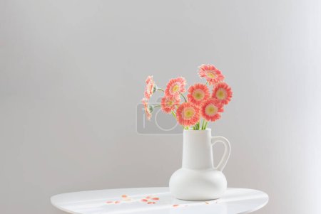 Téléchargez les photos : Gerber rose en cruche blanche sur table blanche - en image libre de droit