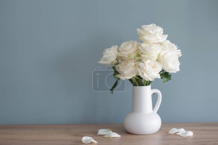 Foto de Ramo de rosas blancas en jarra en la pared de fondo azul - Imagen libre de derechos