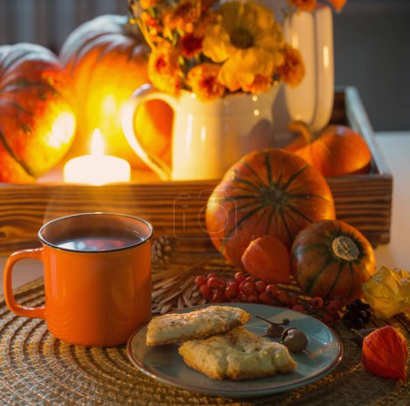Téléchargez les photos : Tasse de thé orange et décor d'automne avec des citrouilles, des fleurs et des bougies allumées sur la table - en image libre de droit