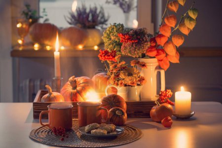 Foto de Dos tazas de té naranja y decoración de otoño con calabazas, flores y velas ardientes en la mesa - Imagen libre de derechos