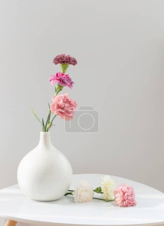 Téléchargez les photos : Belles fleurs d'oeillet dans un vase en céramique sur table blanche - en image libre de droit
