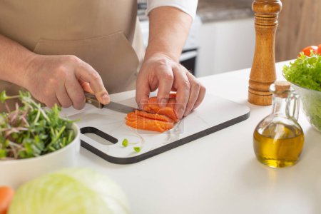 Téléchargez les photos : Homme coupe poivre sur la table dans la cuisine - en image libre de droit