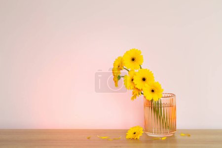 Téléchargez les photos : Gerbera jaune dans un vase en verre sur une table en bois sur le mur de fond - en image libre de droit