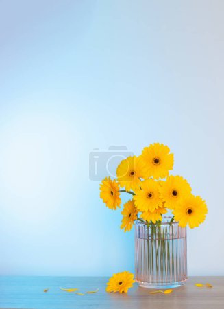 Foto de Gerberas amarillas en jarrón de cristal sobre mesa de madera sobre pared de fondo - Imagen libre de derechos