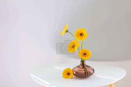 Photo for Yellow gerbera in glass vase on white table on white background - Royalty Free Image