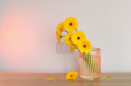 Foto de Gerberas amarillas en jarrón de cristal sobre mesa de madera sobre pared de fondo - Imagen libre de derechos