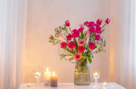 Foto de Flores rosadas en jarrón moderno de cristal con velas encendidas en el interior blanco - Imagen libre de derechos