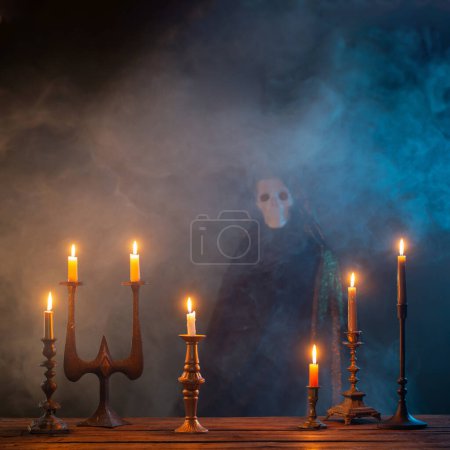 Téléchargez les photos : Grim moissonneuse avec des bougies allumées sur une table en bois dans le fond sombre - en image libre de droit