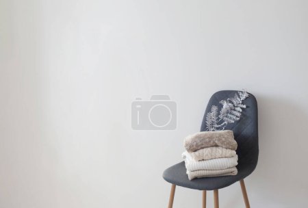Foto de Pila de suéteres en silla moderna gris en habitación blanca - Imagen libre de derechos