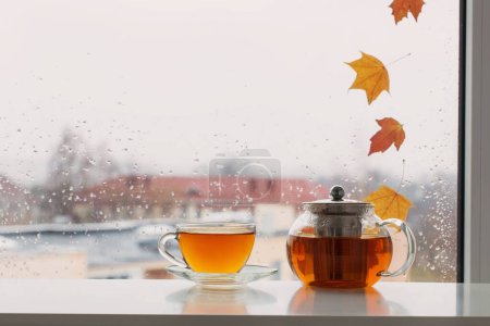 Téléchargez les photos : Tasse de thé sur le rebord de la fenêtre avec des feuilles d'automne sur le panneau de fenêtre - en image libre de droit