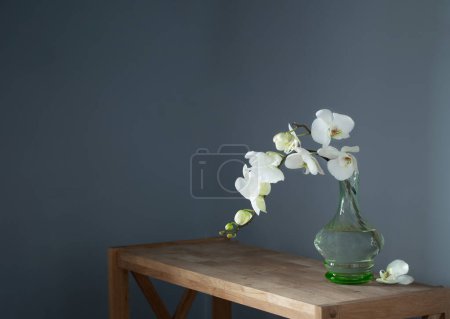 Foto de Orquídea blanca en jarrón de cristal vintage en estante de madera en la pared de fondo - Imagen libre de derechos