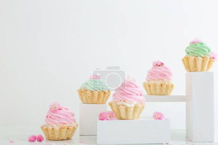 Foto de Cupcakes rosas y verdes con flores de primavera sobre podios de madera sobre fondo blanco - Imagen libre de derechos