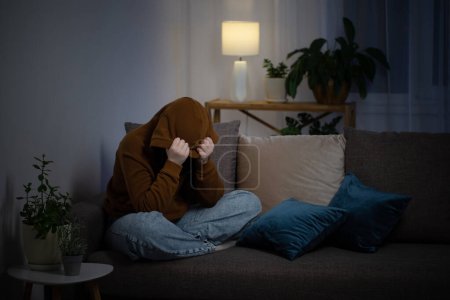 Téléchargez les photos : Triste adolescente assise sur le canapé intérieur la nuit - en image libre de droit