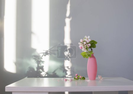 Téléchargez les photos : Branches de pommier avec des fleurs en vase rose sur table blanche - en image libre de droit