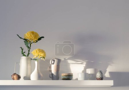 Téléchargez les photos : Chrysanthème jaune dans un vase et des tasses sur étagère blanche sur fond blanc - en image libre de droit
