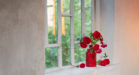 Téléchargez les photos : Roses rouges dans un vase en verre rouge sur le rebord de la fenêtre - en image libre de droit