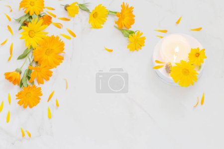 Foto de Flores de caléndula naranja con velas encendidas sobre fondo de mármol blanco - Imagen libre de derechos