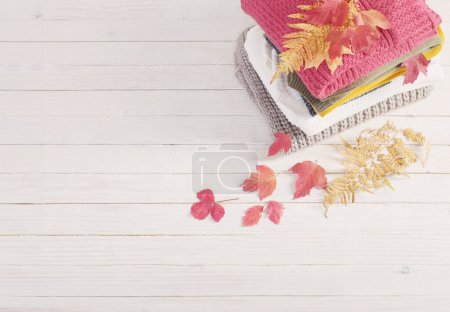 Photo for Stack of sweaters with autumn leaves  on  white wooden table - Royalty Free Image