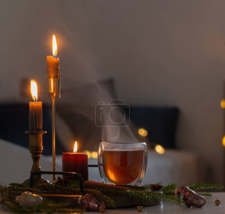 Foto de Té caliente en vidrio termo con decoración de Navidad y velas encendidas en casa - Imagen libre de derechos