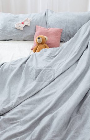 Foto de Cama con osito de peluche en ropa de cama gris - Imagen libre de derechos