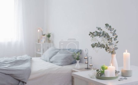 Téléchargez les photos : Bougies allumées et eucalyptus dans un vase dans une chambre blanche - en image libre de droit