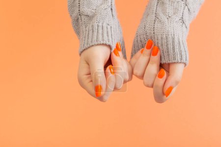 Foto de Manos femeninas con manicura naranja sobre fondo naranja - Imagen libre de derechos