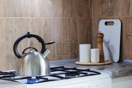 Foto de Hervidor moderno de metal plateado en estufa de gas y utensilios en la cocina - Imagen libre de derechos